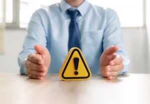 Man in collared shirt and tie sitting at table with warning symbol in front of him