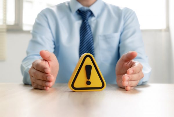 Man in collared shirt and tie sitting at table with warning symbol in front of him