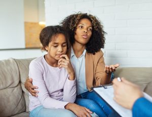 Mother and daughter sitting on a couch as they talk with a therapist