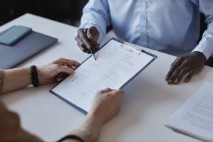 Two people sitting across from each other at a table, reviewing paperwork on a clipboard