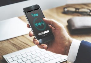 Man sitting at desk looking at his phone with time clearly showing