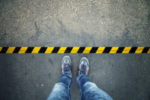 Looking down at a pair of sneaker-clad feet, standing just in front of a yellow and black caution line on the ground