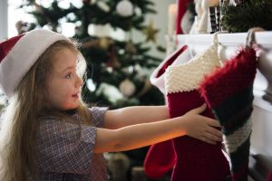 Young girl with brown hair hanging up a Christmas stocking on the mantle