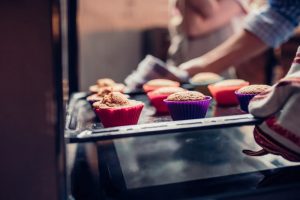 Woman pulling cupcakes out of the oven, focus on cupcakes