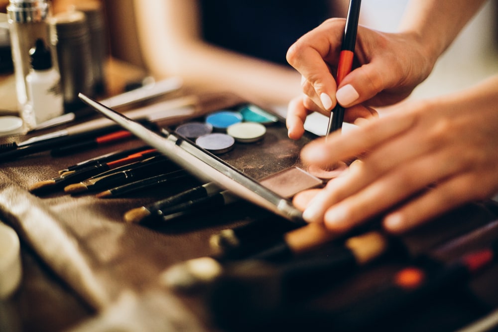 Close-up on woman's hands as she holds a makeup brush and uses it to prepare eye shadow for use