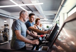 Older man standing on treadmill at gym, getting assistance with setting goals