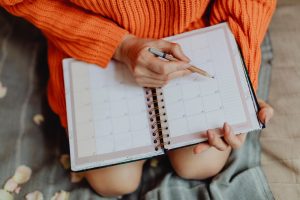 Woman wearing orange sweater as she put together her weekly routine in her calendar planner