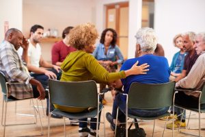 Larger grief support group, listening and offering comfort to a woman who is speaking