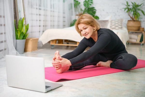 Mature woman sitting on a pink exercise mat, stretching her right leg out in front of her