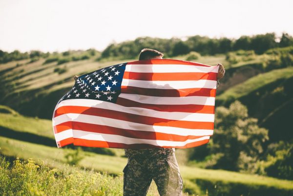 Man in uniform standing outside, holding an American flag