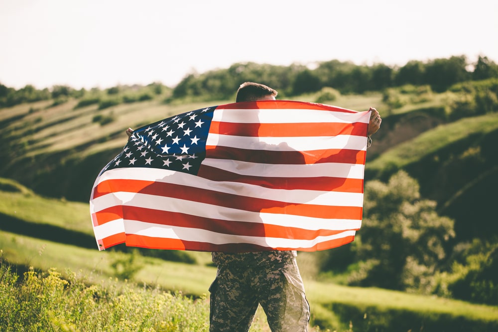 Man in uniform standing outside, holding an American flag