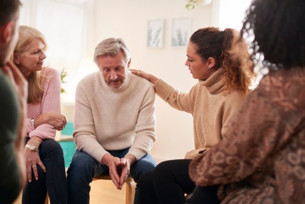 Grief support group meeting; focus on older man receiving comfort from four other members