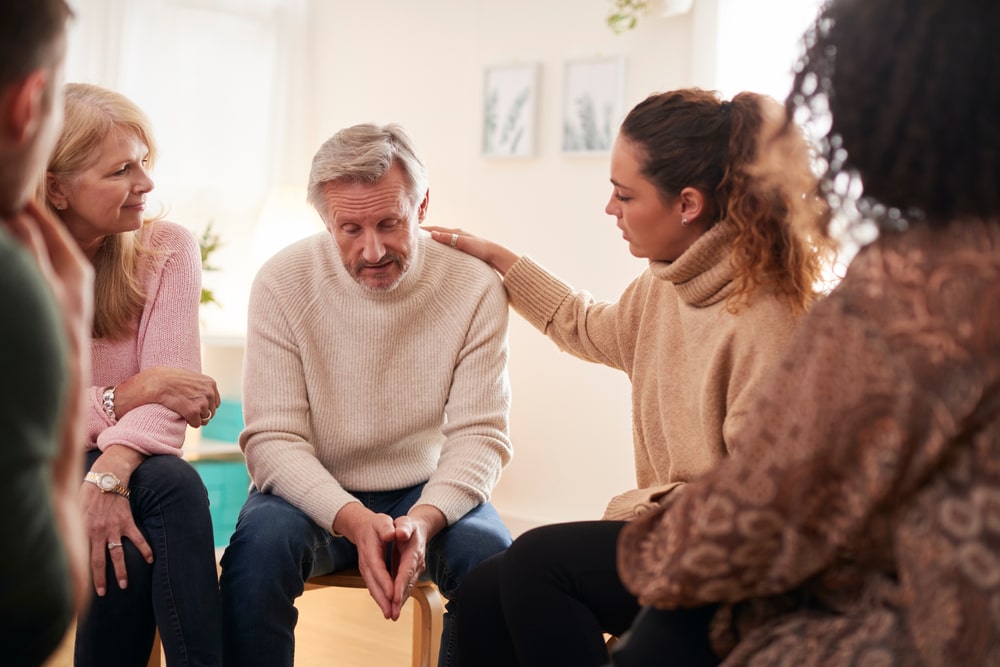 Grief support group meeting; focus on older man receiving comfort from four other members