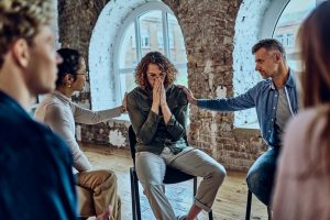 Two people offering support to a young man as he becomes emotional at a grief support group