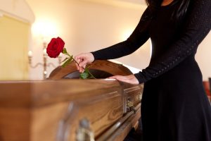 Woman in black dress standing next to an open casket at a viewing, placing a red rose inside the casket