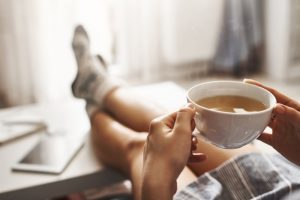Woman sitting at home with a cup of tea, feet resting on coffee table, no stress