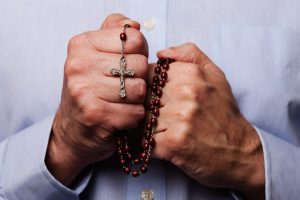 Man in white shirt holding Catholic rosary beads