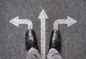 Looking down at a pair of black dress shoes; three arrows indicating different directions to choose; which to choose