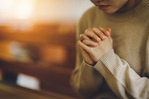 Woman sitting in pew, praying with hands clasped