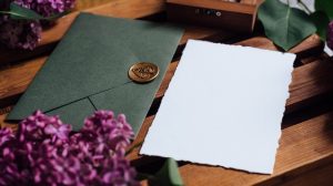 Green envelope and white sheet of paper to use for an honorarium; items are sitting on a table with purple hydrangeas