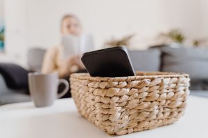 Cell phone put away in a basket as woman takes a social media break; woman sitting on couch reading