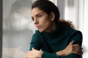 Quiet woman in green sweater sitting at home, thinking and grieving