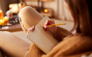 Woman sitting at home, writing in a journal, expressing her thoughts