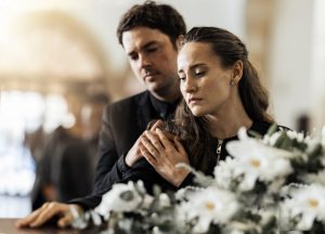 Couple standing next to a casket covered in flowers, paying their respects