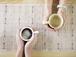 Two people sitting across from each other, each cupping a coffee mug in their hands; aerial view