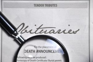 Obituaries in newspaper with magnifying glass