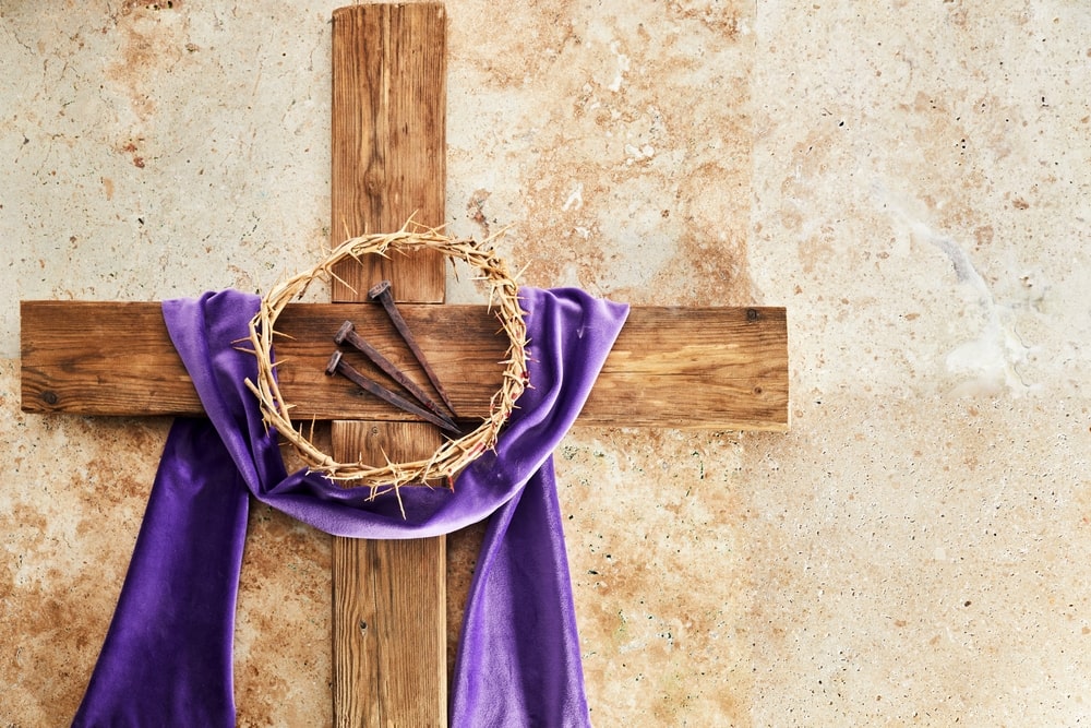 Small wooden cross with purple ribbon, small crown of thorns, and three nails