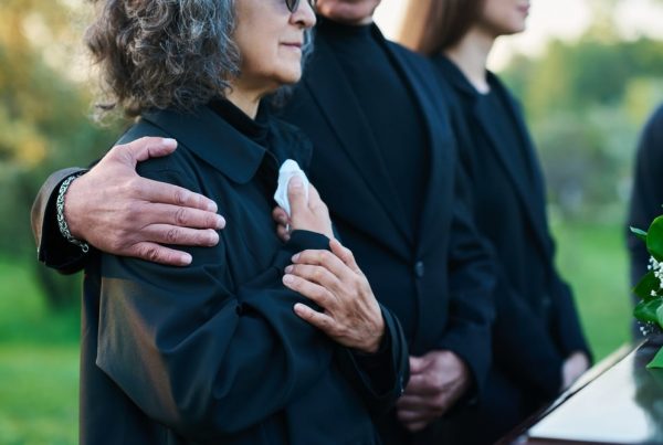 Two women and one man standing at a graveside service, one woman holding a white handkerchief