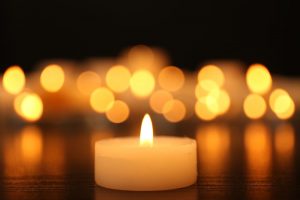 Small lit candle with other candles in the background