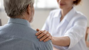 woman putting her hand on an elderly man's shoulder to comfort him