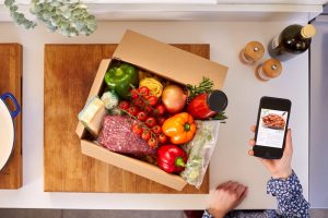 Meal box with ingredients and woman holding the recipe on her phone