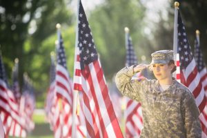 Picture of woman in uniform, standing by American flag and saluting