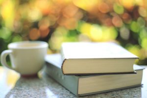 Two hardback books sitting on a table next to a white coffee mug