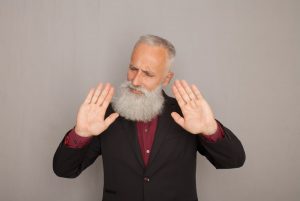 Older man with gray beard holding up hands as he says no to something