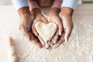 parent and child baking and holding cookie dough in a heart shape