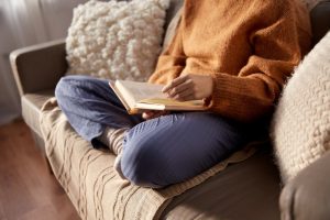 Woman in rust-colored sweater sitting on couch, reading a book