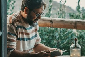 Man sitting at an outdoor table by himself, reading a book of poems