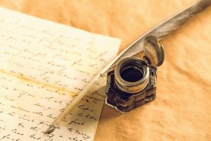 Quill pen and ink bottle next to a stack of handwritten letters