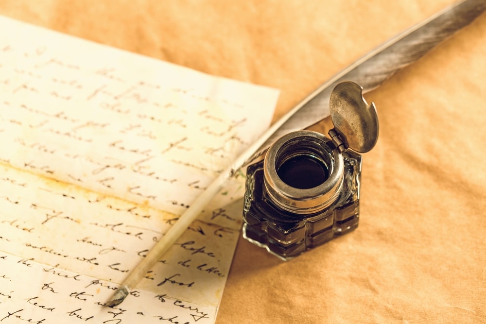 Quill pen and ink bottle next to a stack of handwritten letters