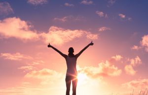 Woman standing in front of a sunrise with her arms raised