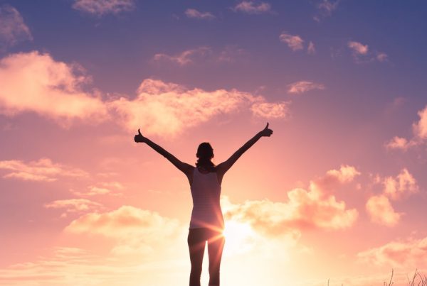 Woman standing in front of a sunrise with her arms raised
