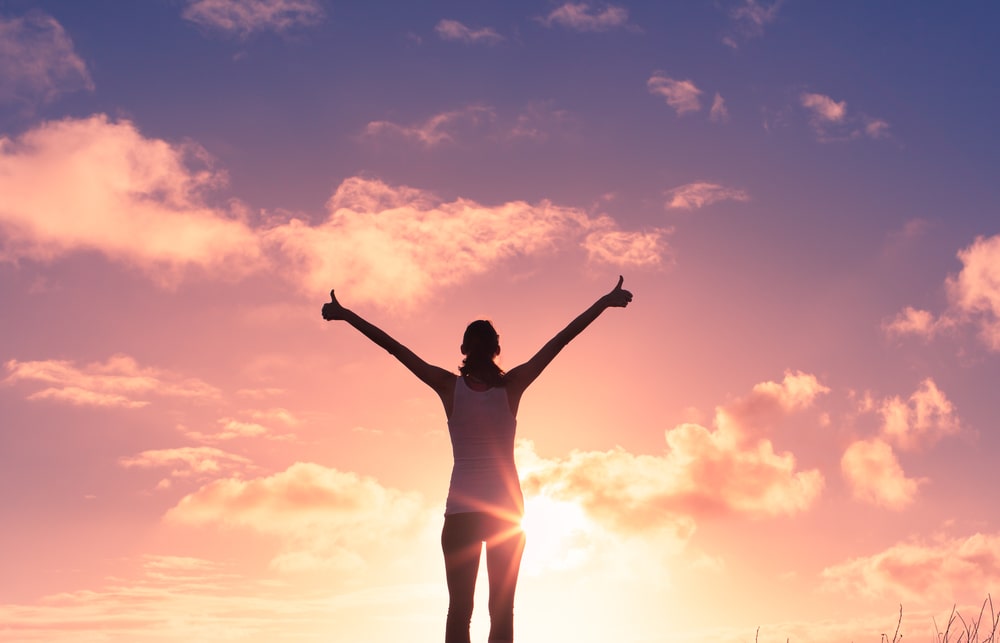 Woman standing in front of a sunrise with her arms raised