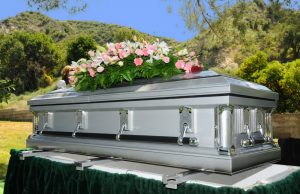 Silver metal casket with pink and white flower spray on top