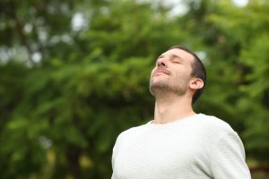 man wearing a white shirt breathing in deeply outside