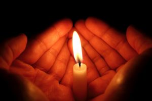 person cupping their hands around a burning candle