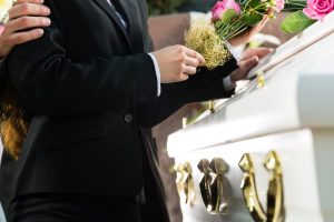 Two people standing by white casket, placing pink flowers on top